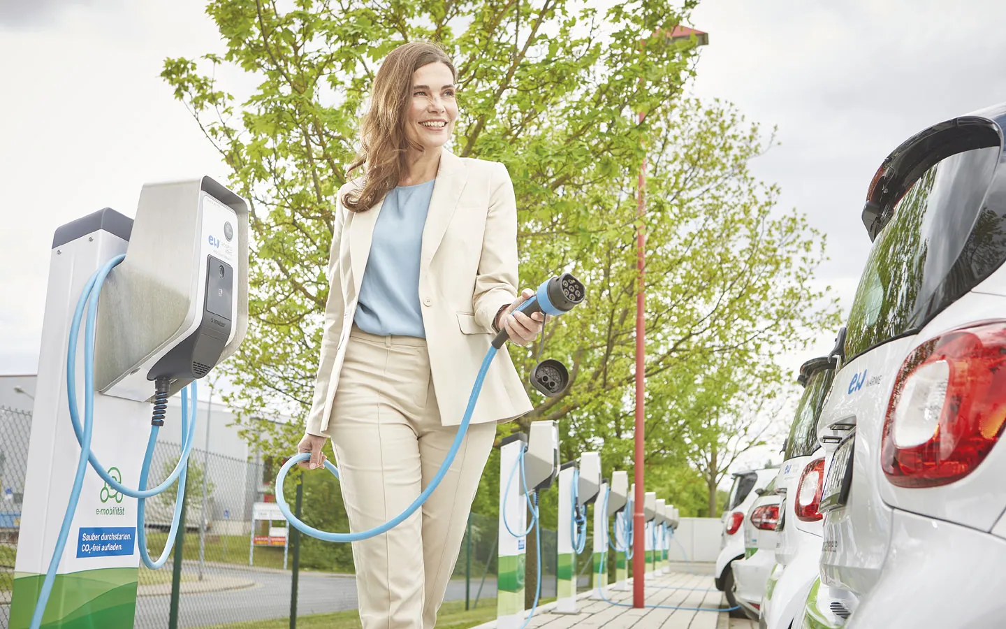 E-Mobilität - Kundin vor Ladestation mit Stecker in der Hand &middot; Winter Elektro